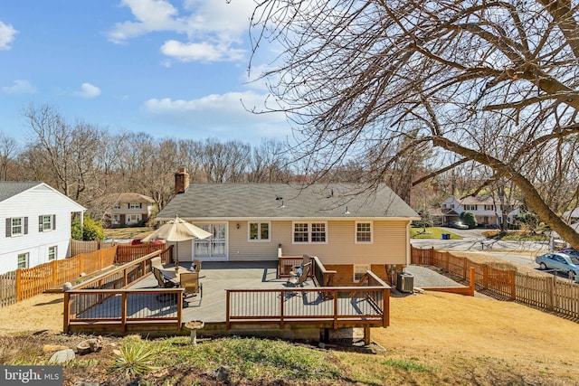 rear view of house featuring brick siding, a wooden deck, cooling unit, a chimney, and a fenced backyard