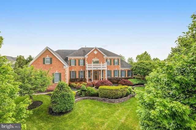 colonial house featuring brick siding, a balcony, and a front lawn