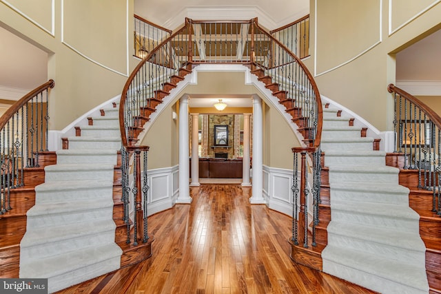 entrance foyer with ornate columns, a decorative wall, ornamental molding, and hardwood / wood-style flooring