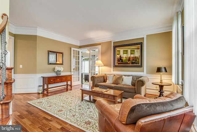 living room featuring a wainscoted wall, wood finished floors, crown molding, and a decorative wall