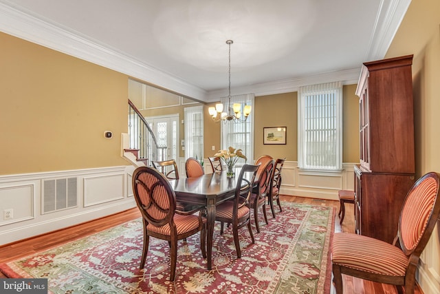 dining space with visible vents, ornamental molding, wood finished floors, an inviting chandelier, and a decorative wall