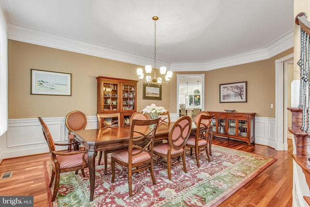 dining room with visible vents, light wood-style floors, wainscoting, crown molding, and a chandelier