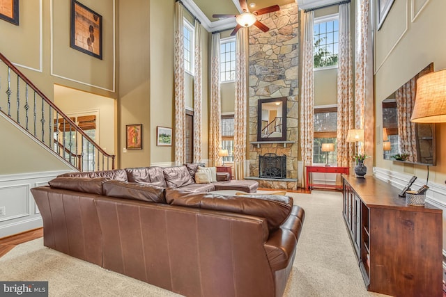 carpeted living room featuring ceiling fan, stairway, a stone fireplace, a high ceiling, and a decorative wall