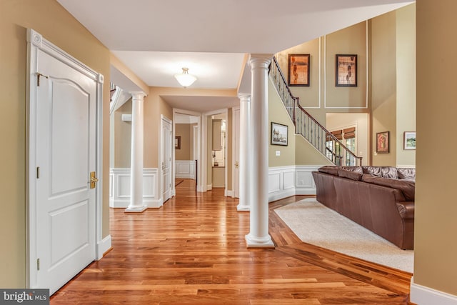 entryway with stairway, light wood finished floors, ornate columns, wainscoting, and a decorative wall