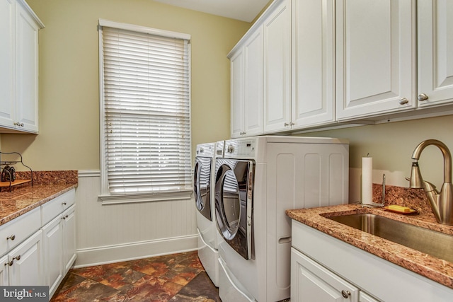 clothes washing area with a wainscoted wall, cabinet space, a sink, stone finish flooring, and independent washer and dryer