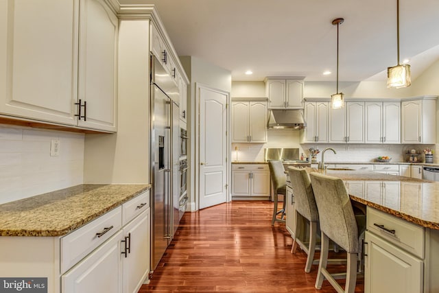 kitchen with under cabinet range hood, dark wood finished floors, light stone counters, a kitchen breakfast bar, and hanging light fixtures