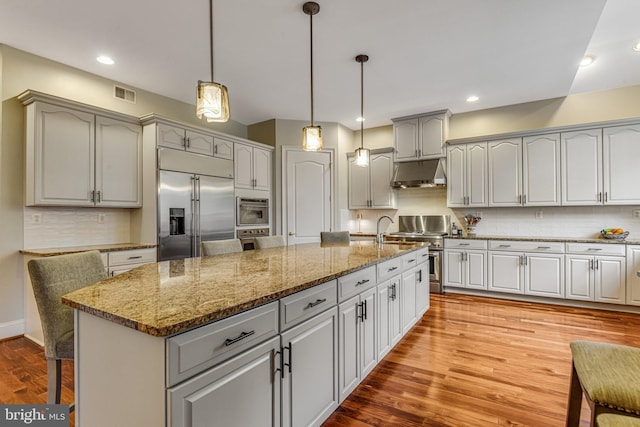 kitchen featuring visible vents, under cabinet range hood, decorative backsplash, wood finished floors, and high end appliances