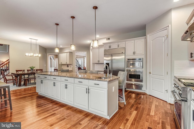 kitchen featuring a warming drawer, a kitchen island with sink, a sink, appliances with stainless steel finishes, and white cabinets