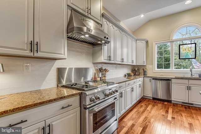 kitchen with under cabinet range hood, a sink, backsplash, stainless steel appliances, and vaulted ceiling