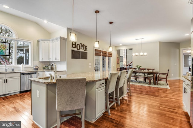 kitchen featuring light wood finished floors, backsplash, dishwasher, an island with sink, and light stone counters