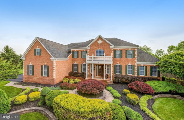 colonial home featuring a balcony, brick siding, and roof with shingles