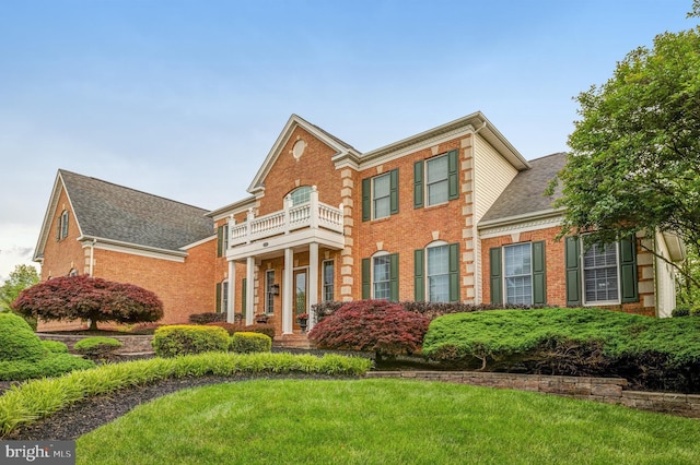 colonial-style house featuring a front lawn, a balcony, and brick siding