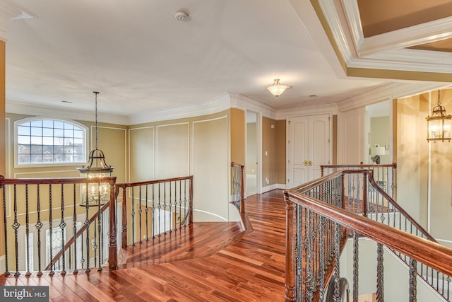 corridor featuring wood finished floors, an upstairs landing, a chandelier, and crown molding