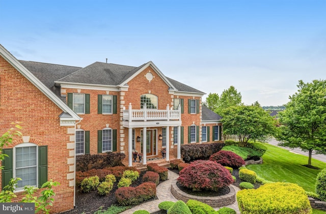 colonial-style house with brick siding, a shingled roof, and a balcony