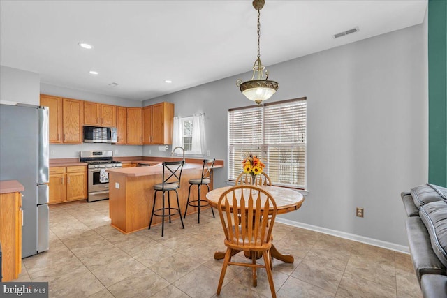 kitchen featuring a breakfast bar area, baseboards, visible vents, a peninsula, and stainless steel appliances