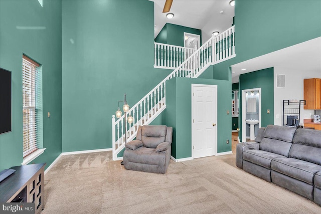 carpeted living area with visible vents, baseboards, a high ceiling, and stairs