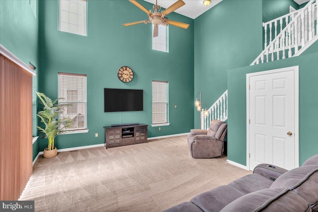 carpeted living room with stairway, ceiling fan, and baseboards