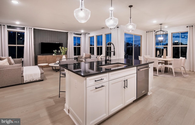 kitchen featuring open floor plan, light wood finished floors, an island with sink, and a sink