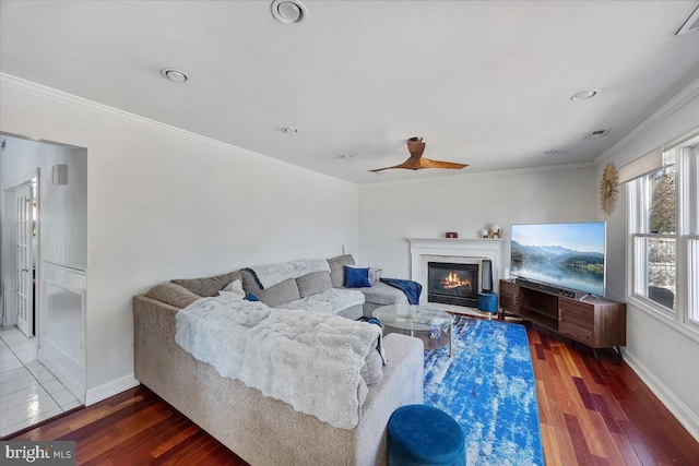 living room with ceiling fan, wood finished floors, baseboards, a glass covered fireplace, and crown molding