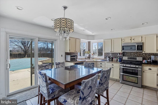 kitchen featuring light tile patterned floors, a sink, appliances with stainless steel finishes, backsplash, and an inviting chandelier