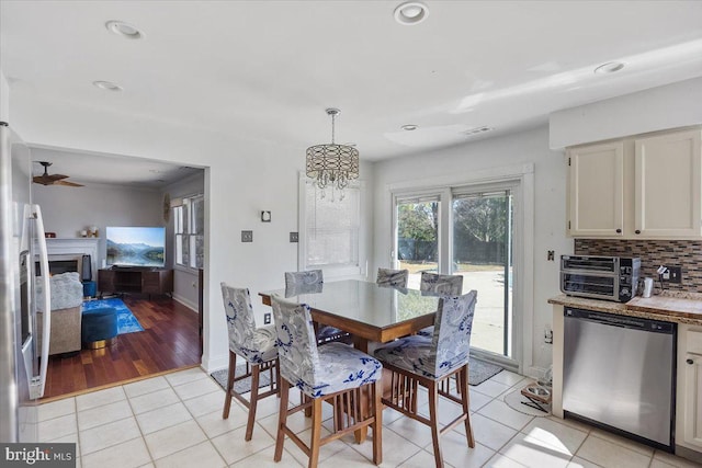 dining space with a toaster, visible vents, light tile patterned flooring, a fireplace, and ceiling fan with notable chandelier