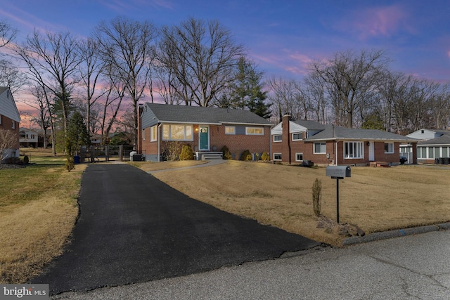 single story home featuring aphalt driveway, a chimney, a front yard, and brick siding
