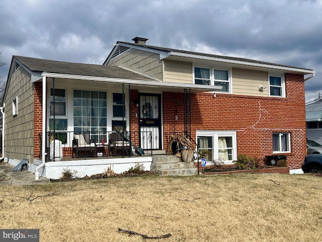 tri-level home with a front lawn, covered porch, and brick siding