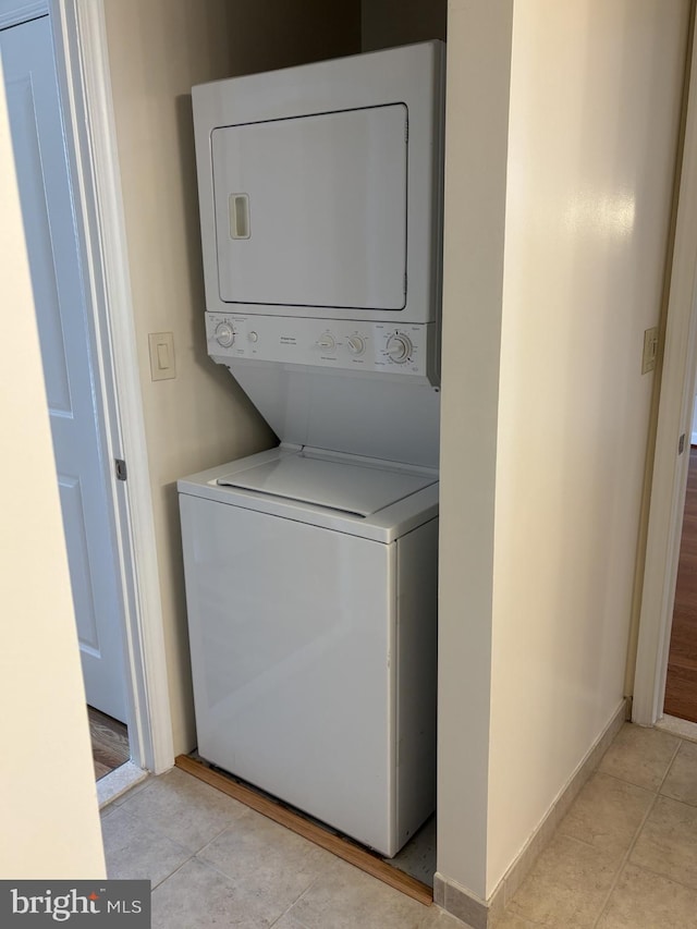 clothes washing area with light tile patterned floors, baseboards, laundry area, and stacked washing maching and dryer