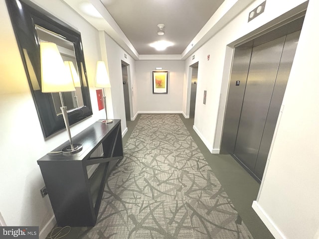 hallway featuring elevator, baseboards, and carpet floors