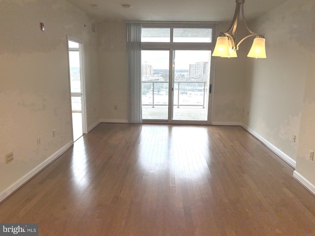 unfurnished room with wood finished floors, baseboards, and a chandelier