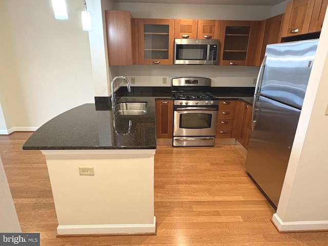 kitchen featuring a peninsula, a sink, light wood-style floors, appliances with stainless steel finishes, and brown cabinets