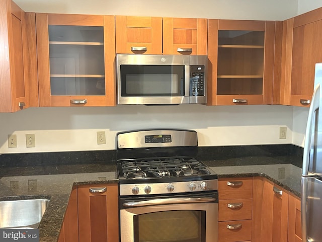 kitchen featuring brown cabinetry, appliances with stainless steel finishes, and glass insert cabinets