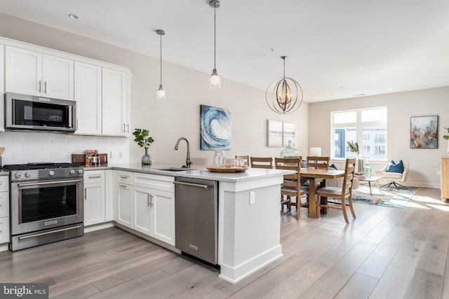 kitchen featuring a sink, light wood-style floors, appliances with stainless steel finishes, a peninsula, and white cabinets