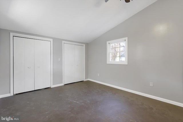 unfurnished bedroom with baseboards, two closets, concrete flooring, and lofted ceiling