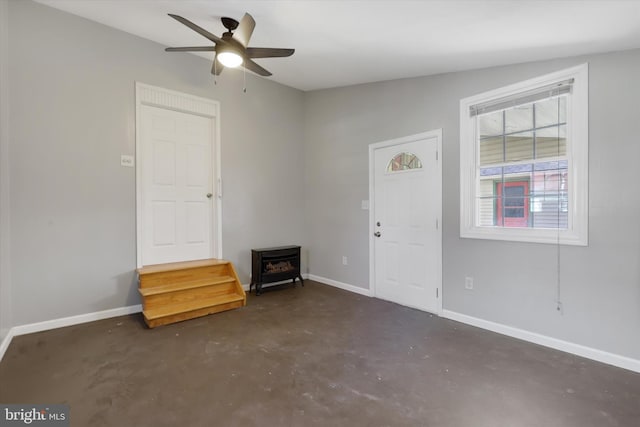 entryway with concrete floors, a ceiling fan, a wood stove, and baseboards