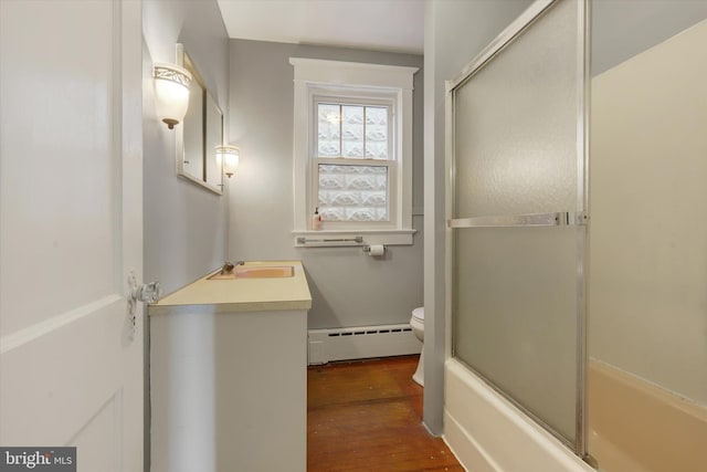 bathroom featuring toilet, wood finished floors, shower / bath combination with glass door, vanity, and a baseboard radiator