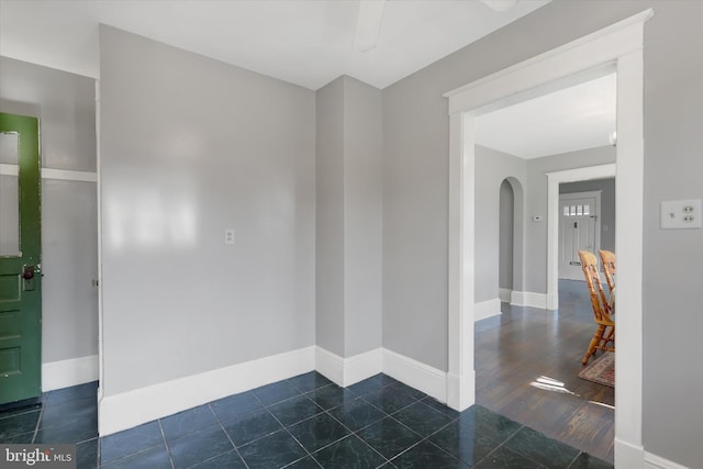 empty room with tile patterned floors, arched walkways, and baseboards