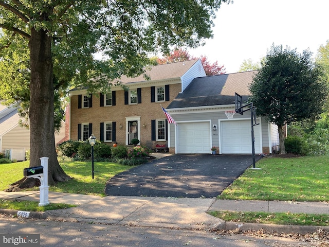 colonial home featuring aphalt driveway, brick siding, a garage, and a front yard