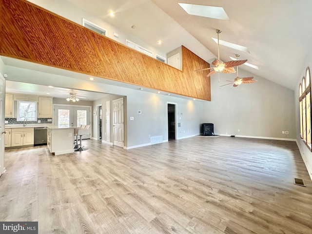 unfurnished living room with light wood-type flooring, a skylight, visible vents, and a wood stove