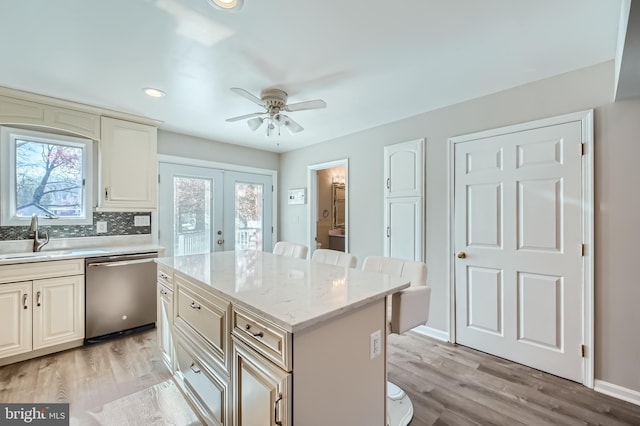 kitchen featuring light wood-style flooring, a sink, stainless steel dishwasher, decorative backsplash, and a center island