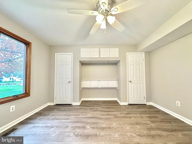 unfurnished bedroom featuring a ceiling fan, visible vents, baseboards, and wood finished floors