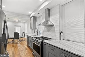 kitchen with stainless steel appliances, gray cabinets, light countertops, a sink, and wall chimney range hood