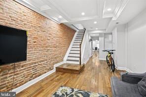 exercise area featuring baseboards, coffered ceiling, brick wall, and wood finished floors