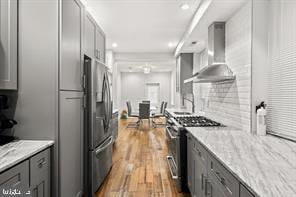 kitchen with light stone counters, gray cabinetry, stainless steel range with gas stovetop, and wall chimney exhaust hood