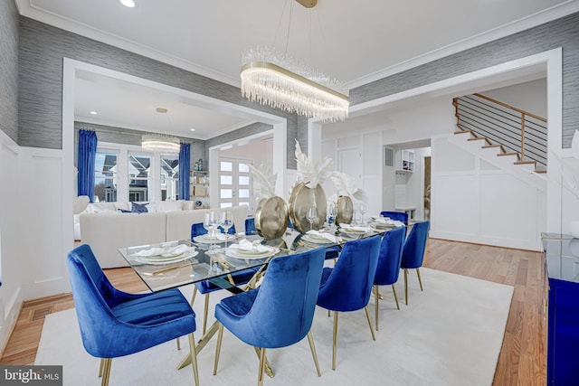 dining room featuring stairs, ornamental molding, wainscoting, wood finished floors, and a decorative wall