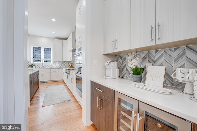 kitchen featuring oven, beverage cooler, white cabinets, light wood finished floors, and decorative backsplash