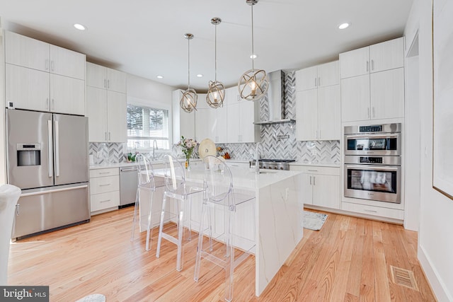 kitchen with visible vents, light wood finished floors, stainless steel appliances, light countertops, and wall chimney exhaust hood