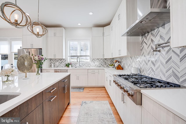 kitchen with light wood-type flooring, tasteful backsplash, appliances with stainless steel finishes, white cabinets, and wall chimney range hood