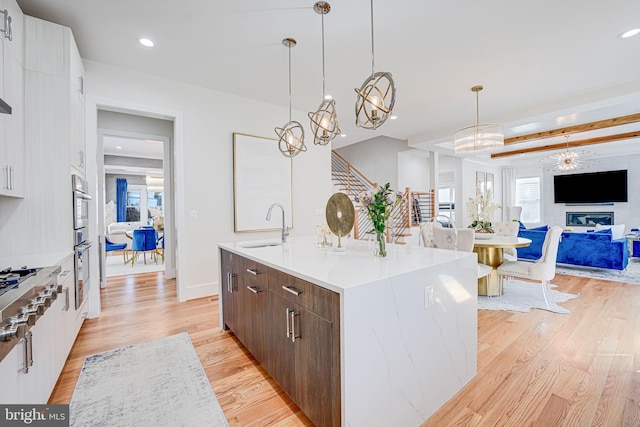 kitchen featuring light wood-type flooring, an island with sink, a sink, recessed lighting, and an inviting chandelier