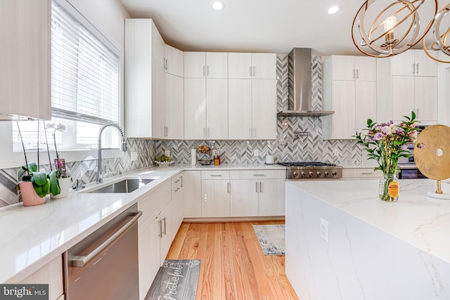 kitchen with a sink, tasteful backsplash, appliances with stainless steel finishes, wall chimney exhaust hood, and light wood finished floors